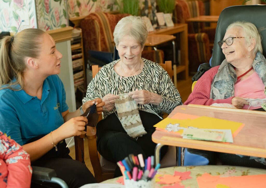 Smiling older adult and a caregiver sitting together at a kitchen table sharing conversation and coffee.