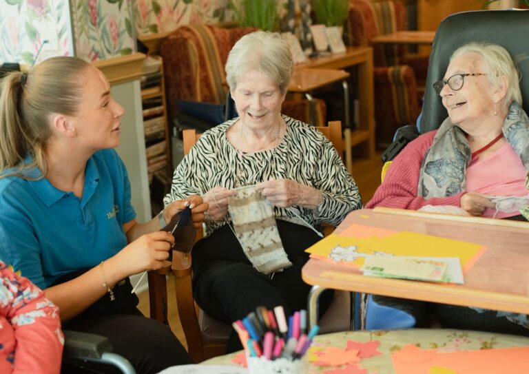 Smiling older adult and a caregiver sitting together at a kitchen table sharing conversation and coffee.