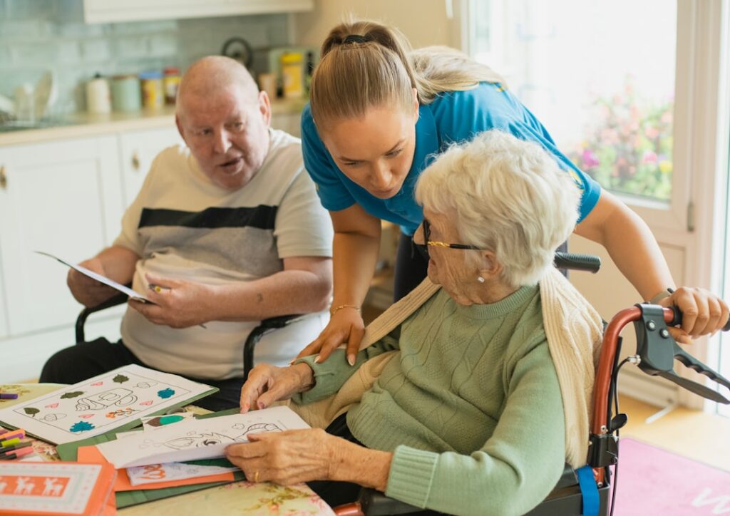 A caregiver helping an older adult with household chores in a sunlit living room.