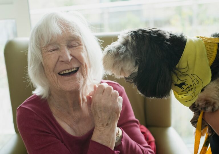 A caregiver and older adult sitting together at a kitchen table sharing conversation and a cup of tea.