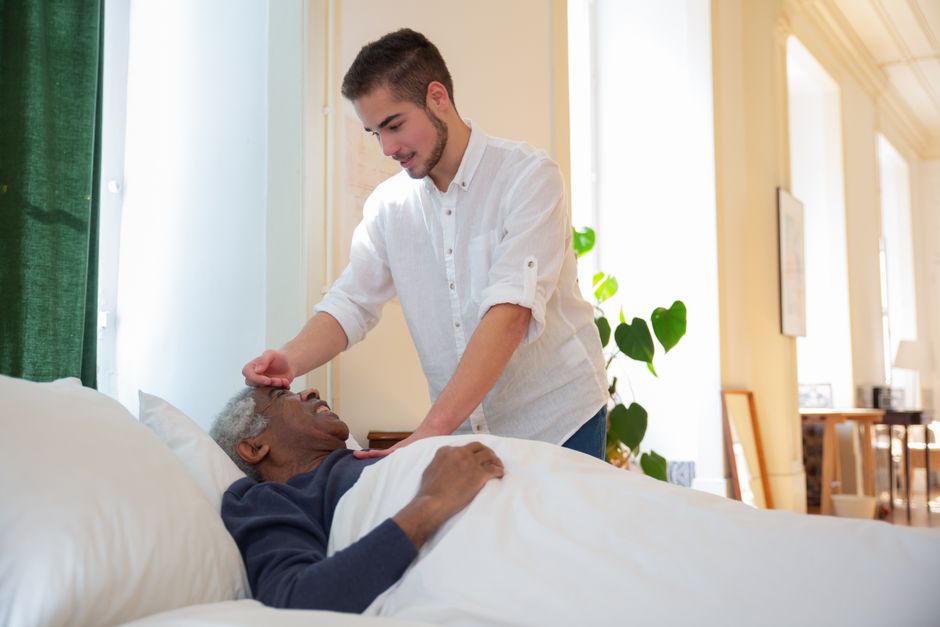 Older adult and caregiver sharing conversation at a kitchen table, with homey background and natural light.