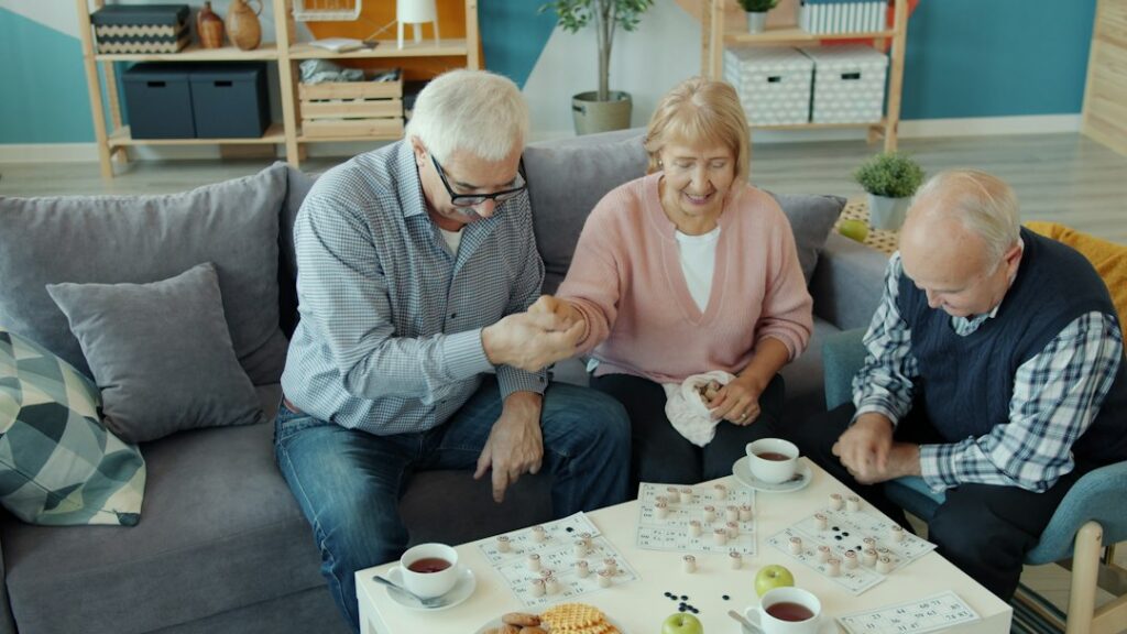An older adult talks with a companion in a bright living room while a family caregiver prepares to leave.